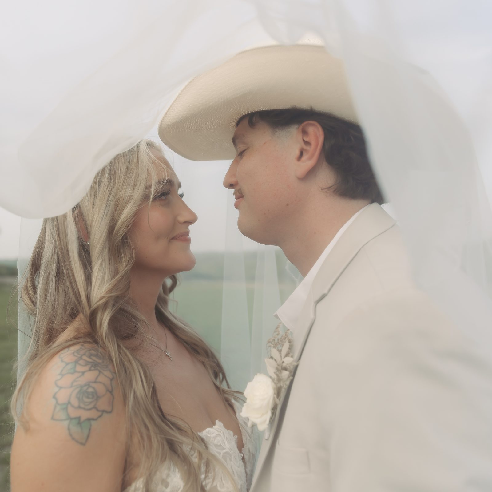 A bride and groom under her veil, foreheads close, looking at each other in an open Hill Country field